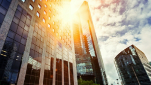 Skyscraper glass facades on a bright sunny day with sunbeams in the blue sky. Modern buildings in business district. Economy, finances, business activity concept. Bottom up view